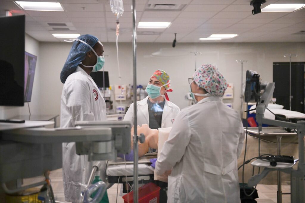 Three Nurse anesthesia students in full mask and gown with gloves working on a simulated patient.