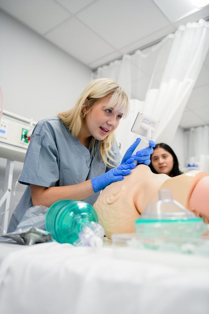 Student Respiratory Therapist in mock hospital room learning to apply respiratory device to a medical simulation plastic mannequin.